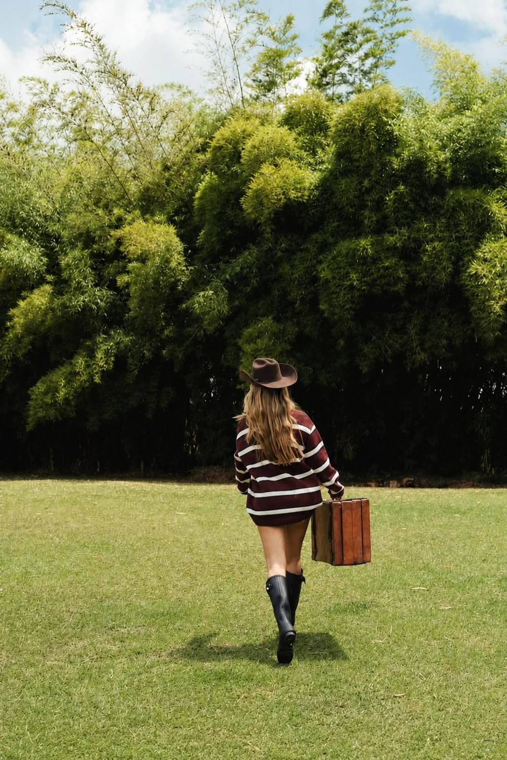 Modelo de espaldas caminando con sombrero de fieltro marrón y maleta de cuero