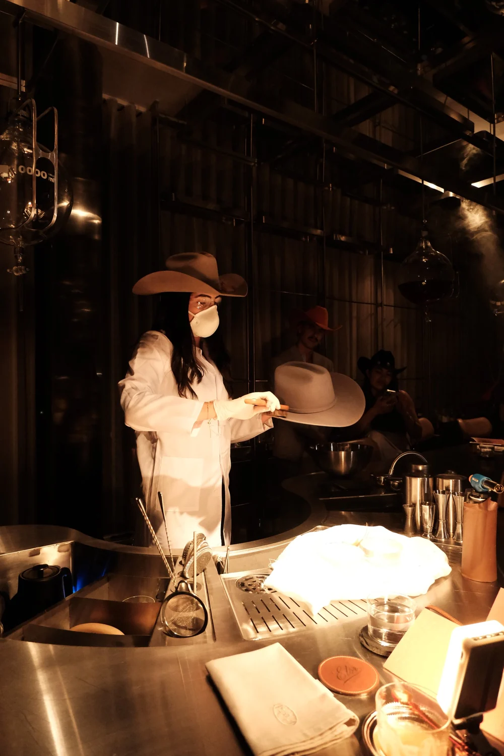 Atelier ELÓR de noche, dos sombreros cream cowboy sobre el counter en luz tungsteno